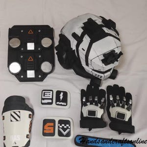 May include: A set of black and white cosplay armour pieces, including a helmet, gloves, and chest plate. The helmet is white with black detailing. The gloves have white and silver details. Several small patches are also included.