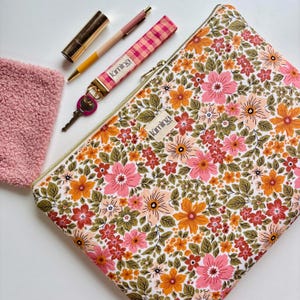 Può includere: Una pochette con cerniera con stampa floreale con cerniera dorata, una chiave rosa, una penna rosa e gialla, un portachiavi a quadri rosa e bianco, una pochette rosa pelosa e un rossetto dorato. La pochette ha un'etichetta bianca con "lúmina".
