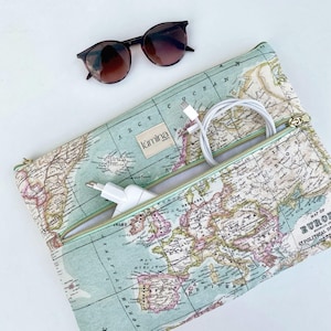 Op de afbeelding: Een reisetui met een vintage kaartontwerp in blauw, groen en roze. De etui is open en onthult een witte oplaadkabel en een voedingsadapter. Een bruine zonnebril ligt erbovenop. De etui heeft een gouden rits.