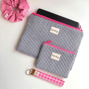 Könnte beinhalten: Eine Auswahl an Accessoires mit einem schwarz-weiß karierten Vichy-Muster und rosa Akzenten. Enthält ein Scrunchie, eine Laptoptasche, eine kleine Reißverschlusstasche und einen Schlüsselanhänger mit Handschlaufe. Jedes Teil hat ein "lúmina"-Etikett.