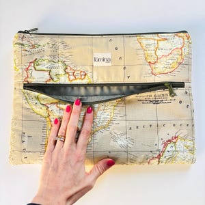 Puede incluir: Bolso de mano beige con estampado de mapa del mundo, cremallera verde oscuro e interior gris claro. La bolsa tiene el nombre de la marca "lumina" en una etiqueta blanca.