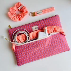 Peut inclure: Un ensemble composé d'une pochette zippée à carreaux vichy violets et orange, d'un chouchou assorti et d'un porte-clés dragonne. La pochette porte une étiquette blanche avec le texte "lumina" et contient un adaptateur secteur et un câble blancs.