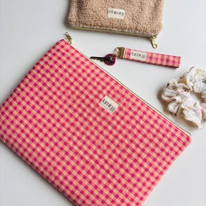 Peut inclure: Ensemble d'accessoires comprenant une grande pochette pour ordinateur portable à carreaux roses et pêche, une petite pochette duveteuse beige, un porte-clés à carreaux roses et un chouchou floral blanc. Chaque article porte l'inscription "lumina".