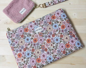 Könnte beinhalten: Ein Set von Accessoires mit floralem Muster, darunter eine große Reißverschlusstasche, eine kleine rosa flauschige Tasche und eine passende Handschlaufe. Das Blumenmuster zeigt Pastellfarben auf weißem Hintergrund. Der Markenname "lumina" ist sichtbar.