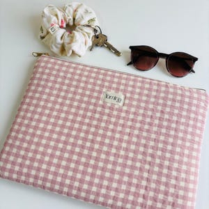 May include: A pink and white gingham laptop sleeve with a zipper closure. The sleeve has a small label that says "tômina" on it.