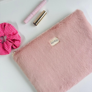 May include: A light pink faux fur cosmetic bag with a gold zipper, a pink scrunchie, a pink mascara tube, and a gold lipstick tube. The bag has a small label that reads "lumina".