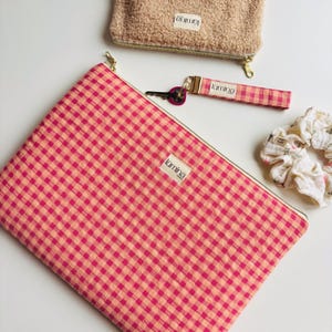 Puede incluir: Una colección de accesorios que incluye una bolsa grande con cremallera a cuadros rosas y melocotón, una pequeña bolsa difusa de color canela, un llavero a cuadros rosas y una scrunchie floral blanca. Cada artículo tiene una pequeña etiqueta blanca con la palabra "lumina".