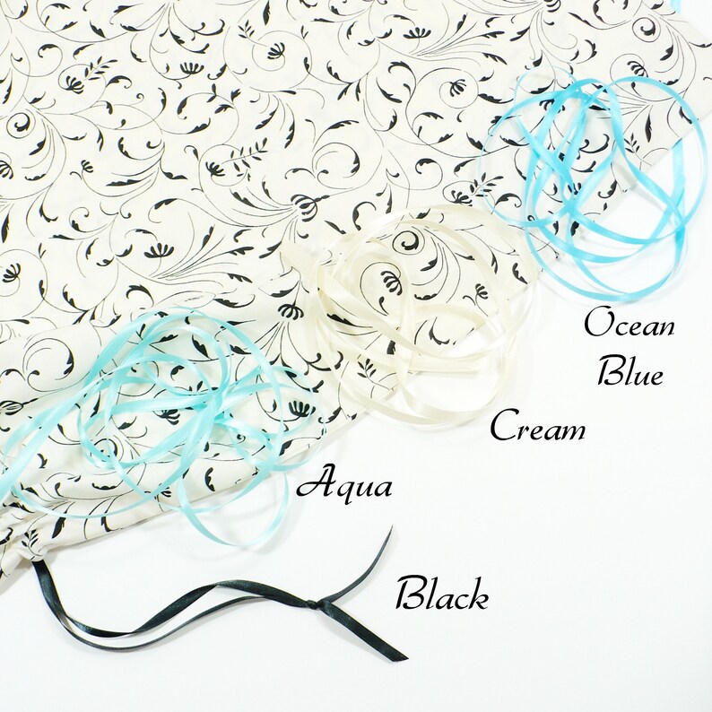 May include: A white fabric bag with a black floral pattern. The bag is decorated with four different colored ribbons: aqua, ocean blue, cream, and black.