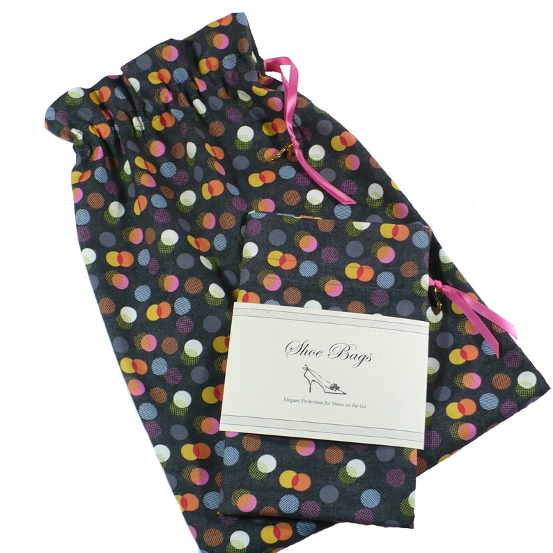 May include: Two black shoe bags with a colorful polka dot pattern. The bags have pink drawstrings and a small tag that reads "Shoe Bags, Elegant Protection for Shoes on the Go."
