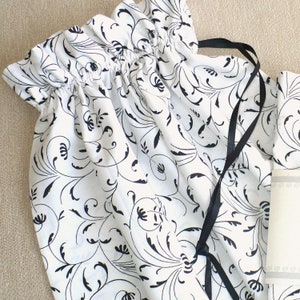 May include: A white fabric drawstring bag with a black and white floral pattern. The bag has a black ribbon drawstring.