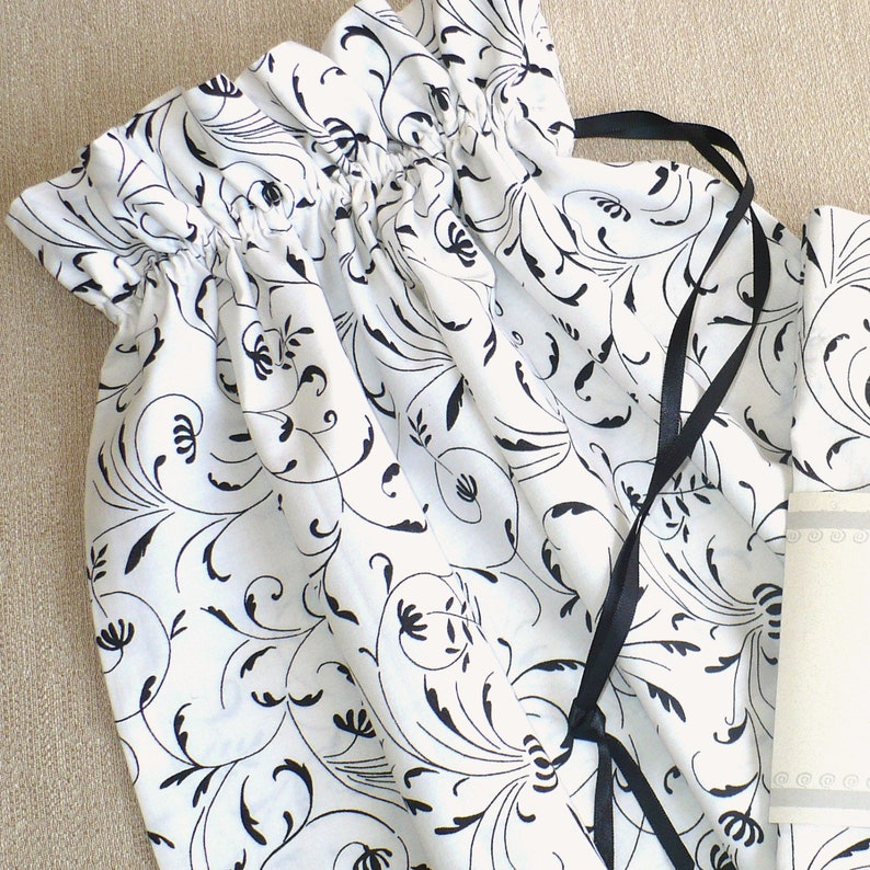 May include: A white fabric drawstring bag with a black and white floral pattern. The bag has a black ribbon drawstring.