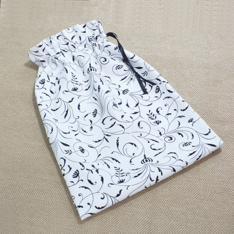 May include: A white drawstring bag with a black floral pattern and a black ribbon drawstring.