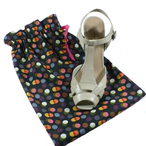 May include: A black and white polka dot shoe bag with a pink drawstring. A beige heeled shoe with a T-strap and the text "INC" is inside the bag.