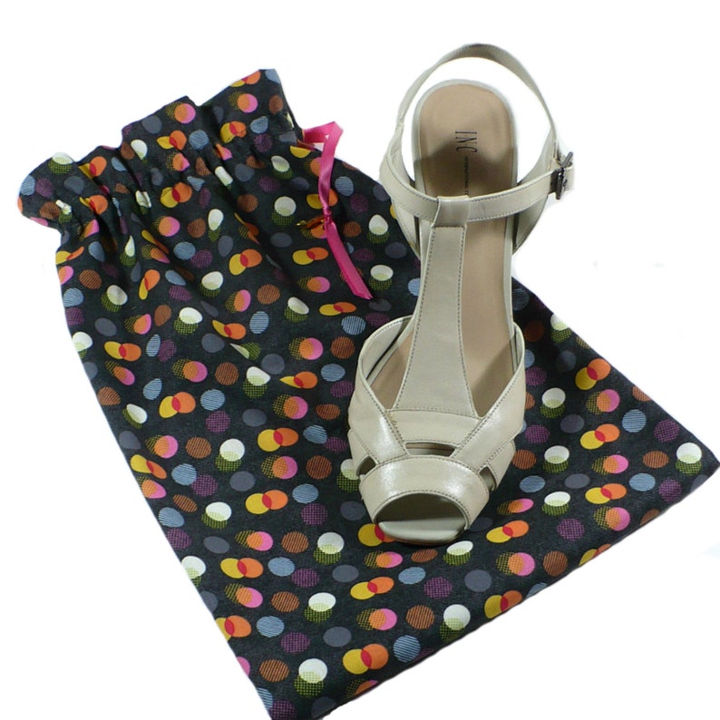 May include: A black and white polka dot shoe bag with a pink drawstring. A beige heeled shoe with a T-strap and the text "INC" is inside the bag.
