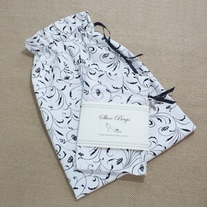 May include: White fabric shoe bags with black floral print and black drawstring ties. The bags have a label that reads "Shoe Bags Elegant Protection for Shoes on the Go."