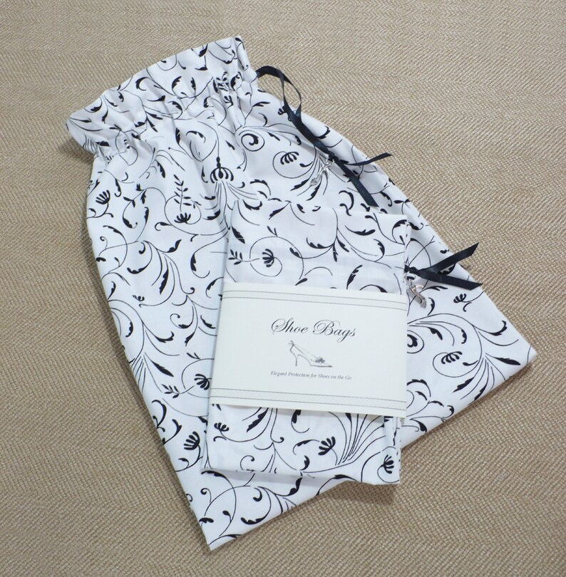 May include: White fabric shoe bags with black floral print and black drawstring ties. The bags have a label that reads "Shoe Bags Elegant Protection for Shoes on the Go."