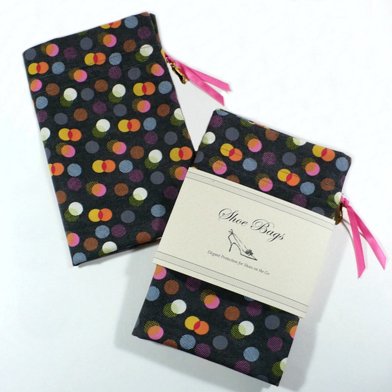 May include: Two black fabric shoe bags with a polka dot pattern in shades of pink, orange, yellow, and blue. The bags have pink drawstrings and a label that reads "Shoe Bags, Elegant Protection for Shoes on the Go."