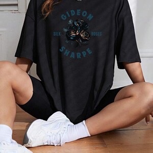 May include: Black oversized t-shirt with a graphic print of a bouquet of blue roses and the text "Gideon Sharpe Silk Roses".