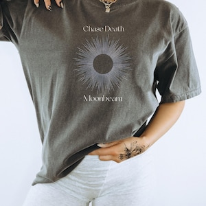 May include: A dark gray t-shirt with a graphic of a sun with rays and the text "Chase Death Moonbeam".