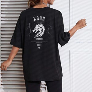 May include: Black oversized t-shirt with a graphic print of a dragon and lightning bolts. The text "KAAN KHAN" and "VAEGOR" is printed on the shirt.