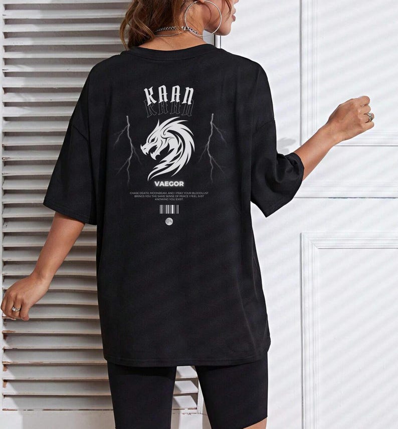 May include: Black oversized t-shirt with a graphic print of a dragon and lightning bolts. The text "KAAN KHAN" and "VAEGOR" is printed on the shirt.