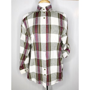 May include: A long-sleeved button-down shirt with a plaid pattern in white, olive green, and grey. The shirt features vertical columns with a repeating geometric design in red and purple. The collar and cuffs have a matching pattern.