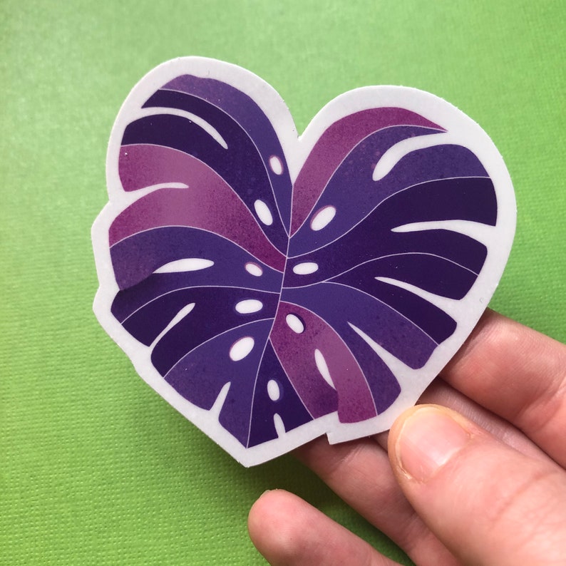 May include: A purple and pink monstera leaf sticker with a white outline. The sticker is shaped like a heart.