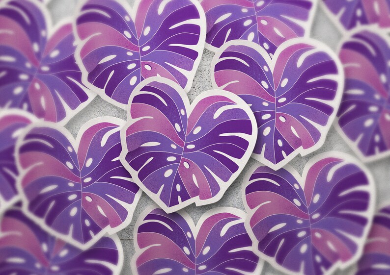 May include: A close-up of multiple purple and pink heart-shaped monstera leaf stickers. The stickers have a textured, watercolor-like finish.