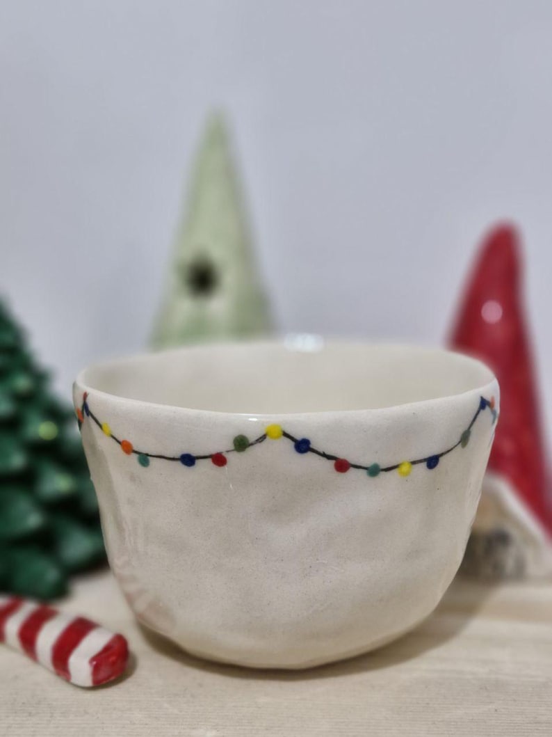 May include: White ceramic bowl with a string of colorful lights painted around the rim. The bowl is slightly textured and has a rounded shape.