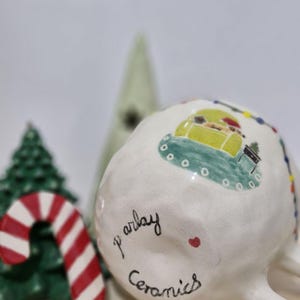 May include: White ceramic mug with a green, yellow, and red Christmas scene painted on the side. The mug has the words "p' arlay ceramics" written on the bottom.