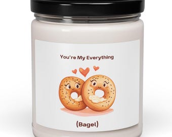May include: A white candle jar with a black lid. The label features two cartoon bagels with smiling faces and the text "You're My Everything" and "(Bagel)" above and below the bagels, respectively. Two orange hearts are above the bagels.