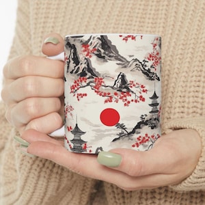 May include: White ceramic mug with a Japanese-inspired design featuring black and gray mountains, red cherry blossoms, and a red sun. The design is repeated across the mug.
