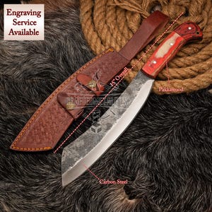 May include: A 15-inch carbon steel knife with a pakkawood handle and a brown leather sheath. The knife has a curved blade and a red and white handle. Engraving service available.
