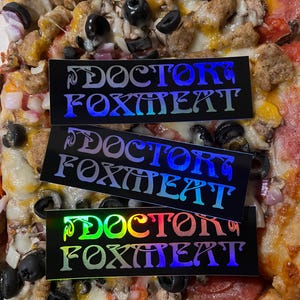 May include: Three iridescent stickers with the text "Doctor Foxmeat" on a black background. The stickers are on a pizza with pepperoni, mushrooms, olives, and cheese.