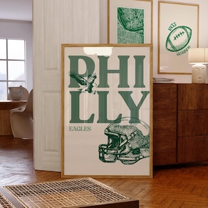 May include: A framed poster with a green and white design. The poster features the word "PHILLY" in large green letters, an eagle, and a football helmet. The word "EAGLES" is printed below the word "PHILLY". Two other framed posters are visible in the background.
