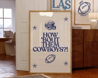 May include: A framed print with the text "HOW 'BOUT THEM COWBOYS?!" in navy blue, along with a football helmet, football, and star graphics. The print is displayed in a room with other framed art and wooden furniture.