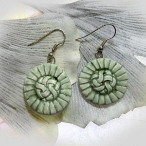May include: A pair of green and silver earrings with a circular design. The earrings feature a woven pattern in the centre.