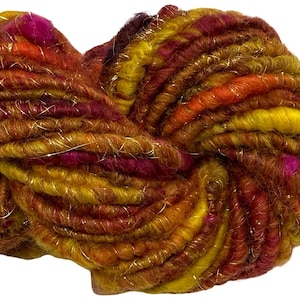 May include: A skein of thick, textured yarn featuring a variegated color palette of mustard yellow, burnt orange, deep burgundy, and magenta. The yarn is twisted with a thin, metallic gold thread that runs throughout the entire length of the fibers.