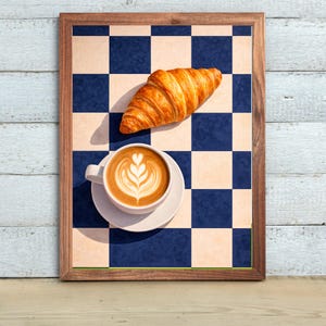 May include: A framed print featuring a croissant and a cup of coffee with latte art on a blue and white checkered background. The coffee cup sits on a white saucer. The croissant is golden brown.