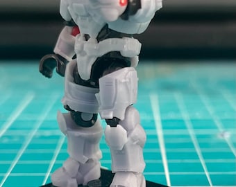 May include: A gray action figure of a futuristic soldier, with detailed armor and a helmet. The figure is posed on a black base, with a red accent on the chest. The figure is made of plastic.