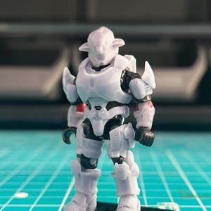 May include: A white plastic action figure of a robot wearing armor with red accents. The figure is standing on a black base.