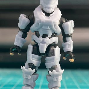 May include: A white plastic action figure of a soldier wearing a helmet and armor. The figure is standing on a small black base.