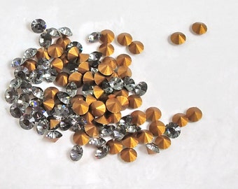 May include: A pile of gold and clear rhinestones. The rhinestones are faceted and have a rainbow effect.