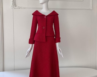May include: A red tweed skirt suit displayed on a mannequin. The suit features a jacket with a unique collar and button closure, paired with a matching knee-length skirt. The fabric has a textured appearance, and the suit is a vibrant shade of red.