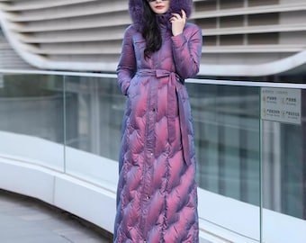 May include: A long, iridescent purple puffer coat with a fur-lined hood and a matching belt. The coat is buttoned up and reaches the ankles. The person is wearing black sunglasses and black pointed-toe boots.