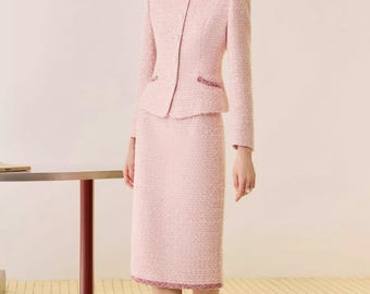 May include: A light pink tweed skirt suit. The jacket has a round neckline, long sleeves, and a peplum waist. The skirt is knee-length. The suit is trimmed with a darker pink detail. Matching pink heels complete the outfit.