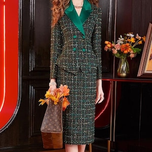 Può includere: Un tailleur gonna in tweed verde con un blazer doppiopetto e una gonna abbinata al ginocchio. Il blazer ha un risvolto in raso verde a contrasto. L'outfit è abbinato a tacchi bianchi e una borsa marrone.