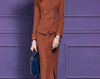 May include: A brown skirt suit with a double-breasted blazer and a knee-length pencil skirt. The blazer has gold buttons and decorative trim. The suit is paired with white heels and a blue handbag.