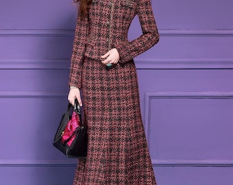 May include: A two-piece tweed suit in a burgundy and black plaid pattern. The jacket has a round neckline, long sleeves, and a front zipper. The skirt is a midi length, flared style. A black handbag with a pink scarf is held in the hand.