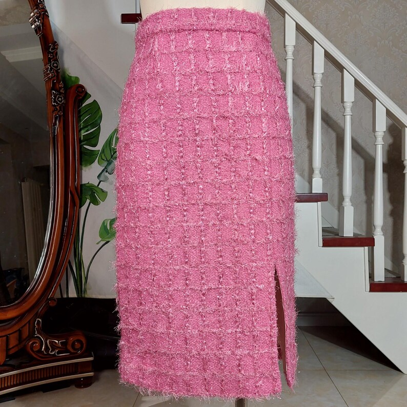 Pu&ograve; includere: Gonna a tubino in tweed rosa con spacco frontale. La gonna &egrave; esposta su un manichino. Il tessuto ha un aspetto strutturato e tessuto. La gonna &egrave; lunga fino al ginocchio e ha un design classico e su misura.